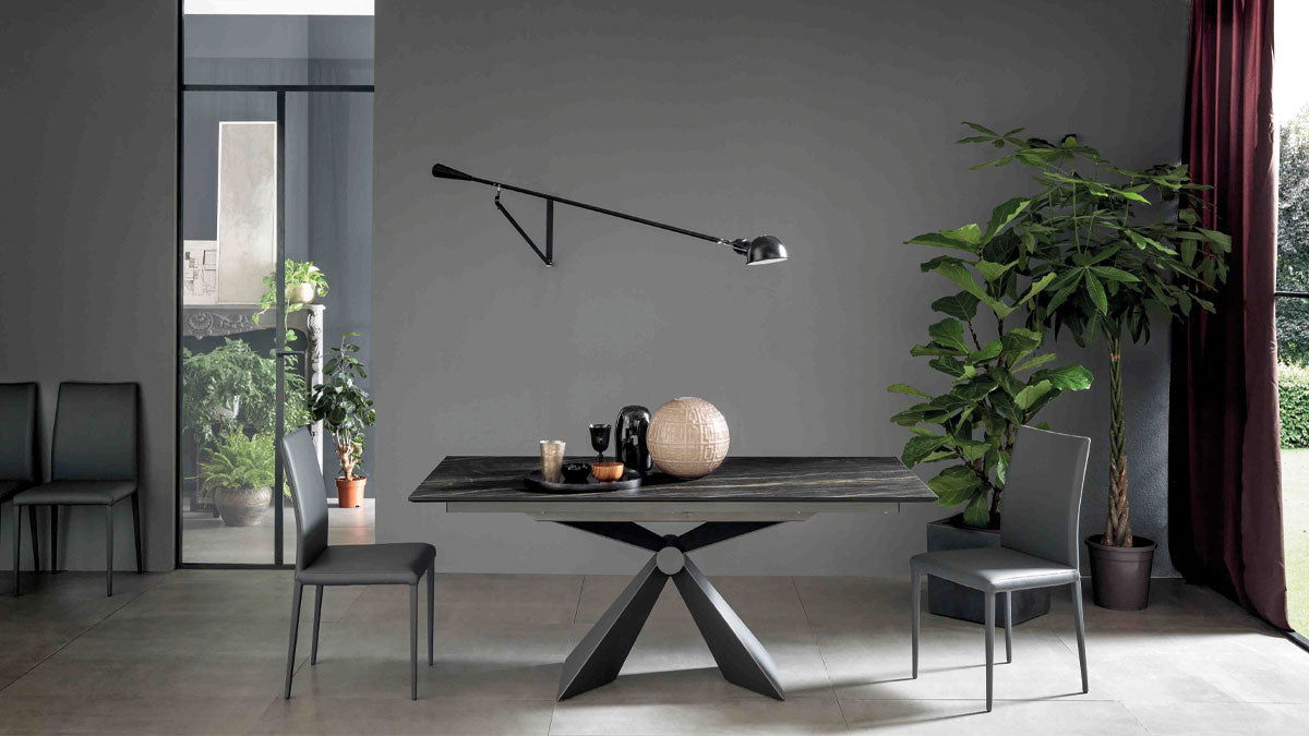 Table extensible Sintesi fermée, plateau céramique effet marbre noir veiné et pied central en métal, dans une salle à manger