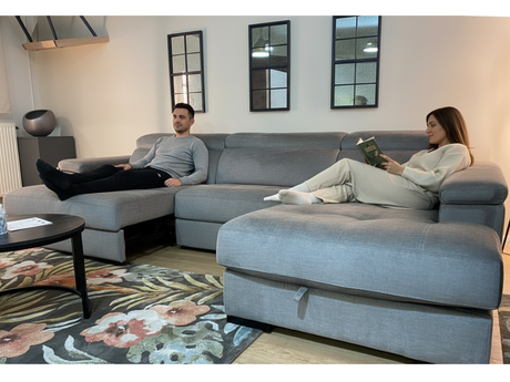Couple se relaxant sur le canapé d'angle Maggy en velours gris - homme utilisant l'assise coulissante déployée, femme sur la méridienne